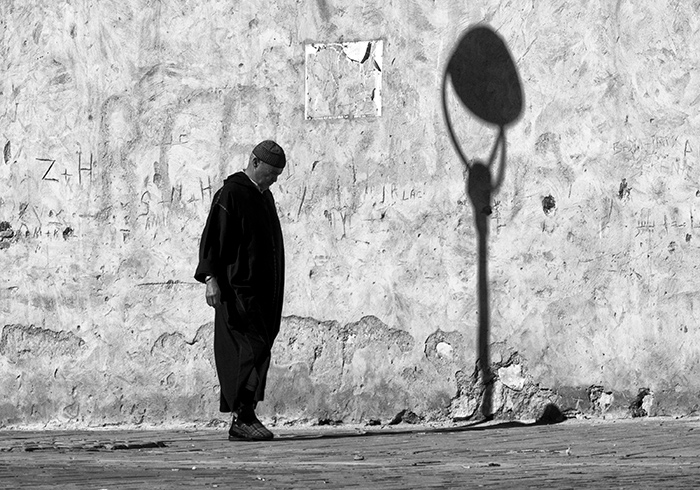 Man with head bowed walks past a lamp post with the appearance of a bowed head